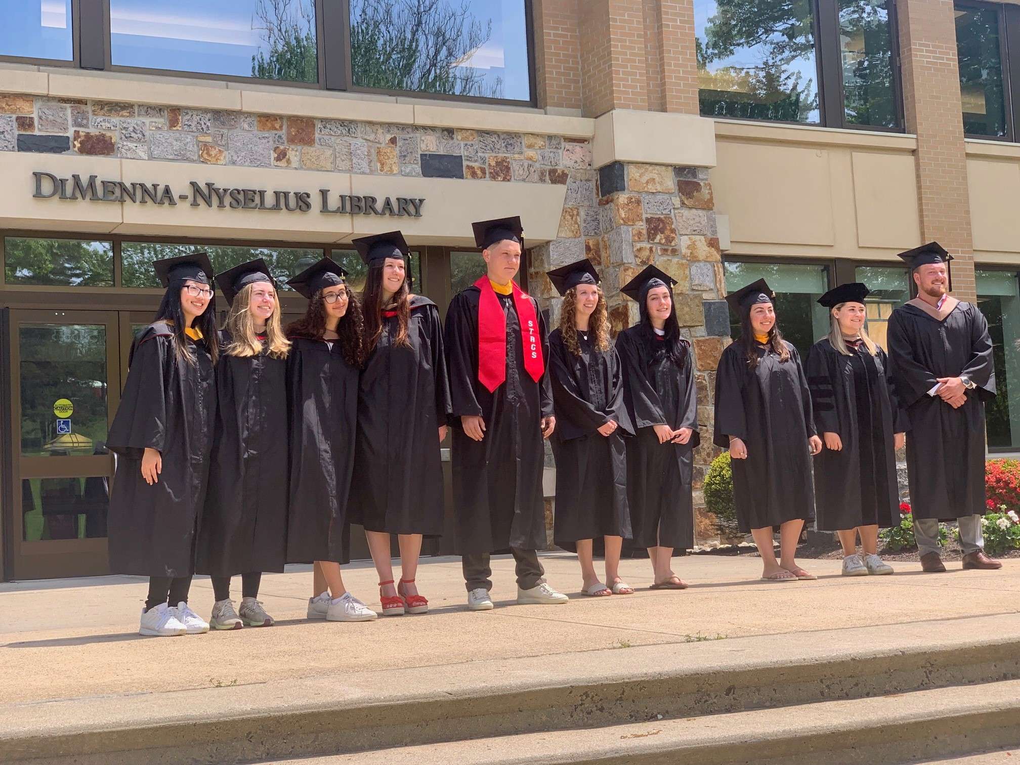 Library student workers, class of 2024, standing in front of the Library in their cap and gowns.