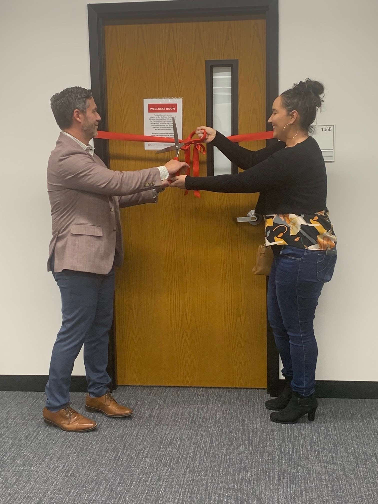 Martin Pino and Melina Calle cut the ribbon with large scissors to the door of the new Wellness Room in the library